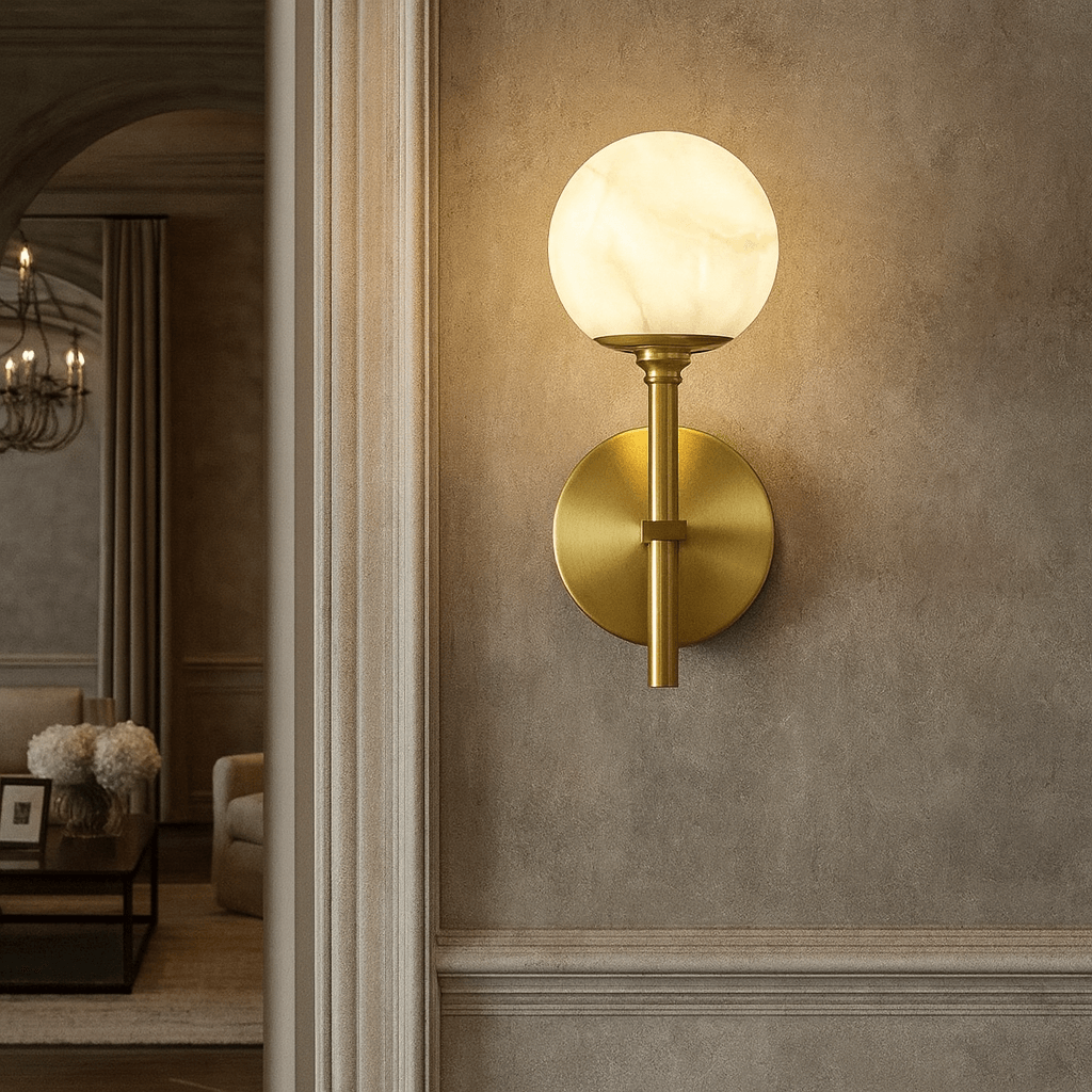 The Aria Copper & Marble Wall Sconce by Morsale, featuring a round frosted glass shade, is mounted on a beige textured wall with an elegant living room, chandelier, and floral arrangement in the background.