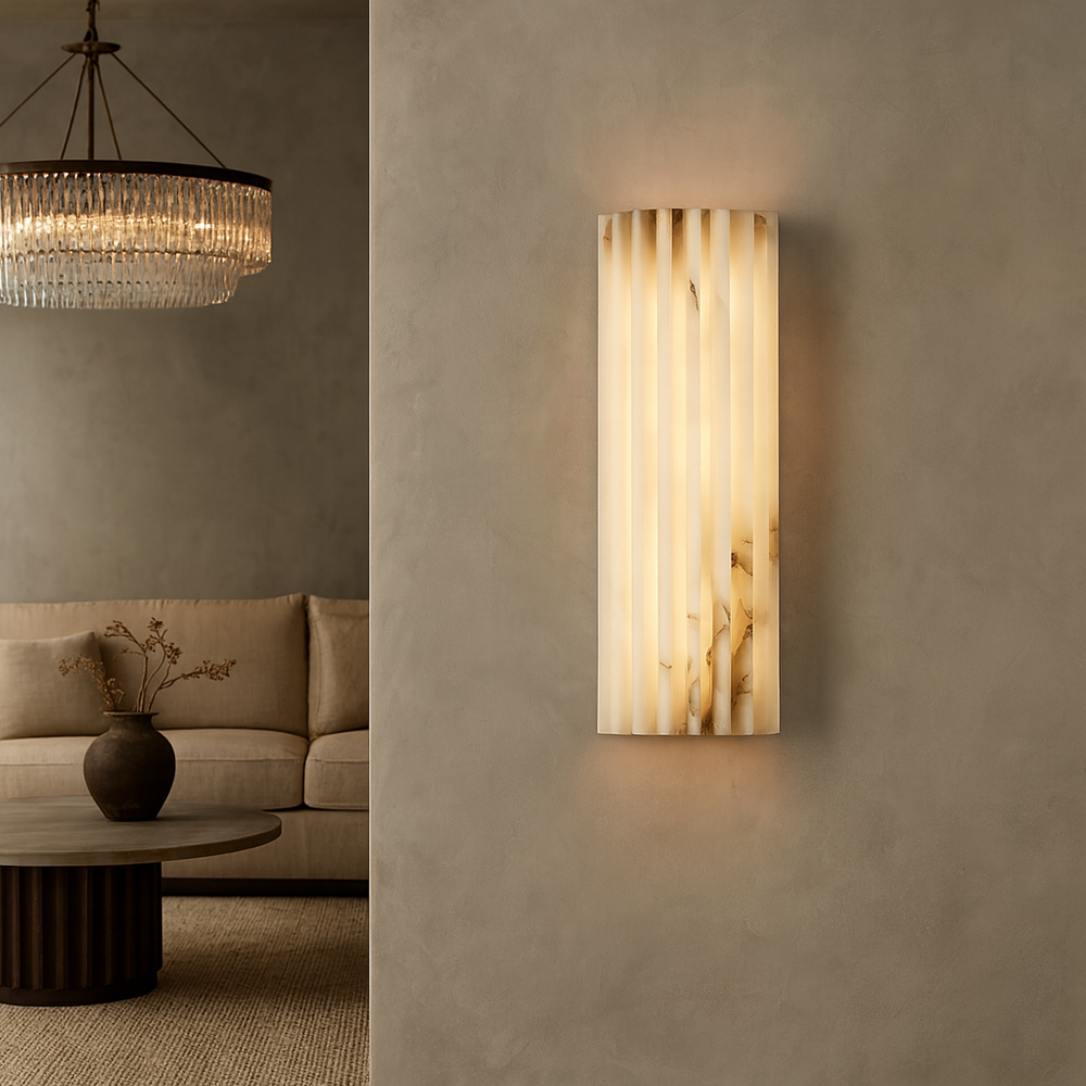 
                  
                    A modern living room showcases a beige sofa, a round wooden coffee table with a dark vase, a large crystal chandelier, and the Morsale Marlo Marble Wall Sconce 12" casting warm light on a textured wall.
                  
                