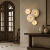 A minimalist entryway with a wooden door, chair, dark console table topped with ceramic vases, and the Solena Marble Disc Wall Sconce from Morsale.com—an elegant fixture with four softly glowing circles for a modern touch.