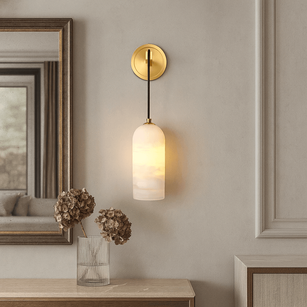 
                  
                    The Lucera Marble Pendant Sconce by Morsale, featuring a gold base and frosted glass shade, casts a warm glow above a table with a clear vase of dried hydrangeas against an elegant, light-toned wall with decorative molding.
                  
                