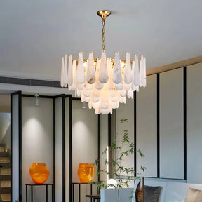 A modern living room showcases the Moonshade Marble Chandelier by Morsale, featuring teardrop-shaped glass pieces and LED bulbs. The space embraces a minimalist design with two orange vases and a small plant on a table, while the walls display a subtle panel pattern that enhances the modern style.