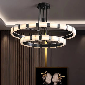 A Morsale.com Villa Marble Mid-Century Modern Chandelier with two circular, double-layered light rings hangs from the ceiling of a contemporary room with wooden panel walls. Below it, a framed artwork depicting two heads with butterflies is displayed against a dark background.