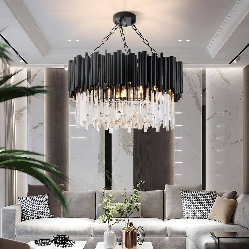 A modern living room with a sleek, contemporary Vigo Collection Crystal Chandelier from Morsale.com hanging from the ceiling. The chandelier features black rods and crystal-like accents. The room has a grey sectional sofa adorned with patterned cushions, a coffee table with decorative items, and elegant wall panels.