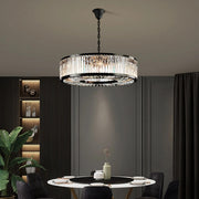 Elegant dining area with a round table set for two beneath the Gio Crystal Modern Chandelier from Morsale.com, adding luxury. Shelves display decorative items and a potted plant enhance ambiance. Dark-toned walls and curtains complete the sophisticated look.