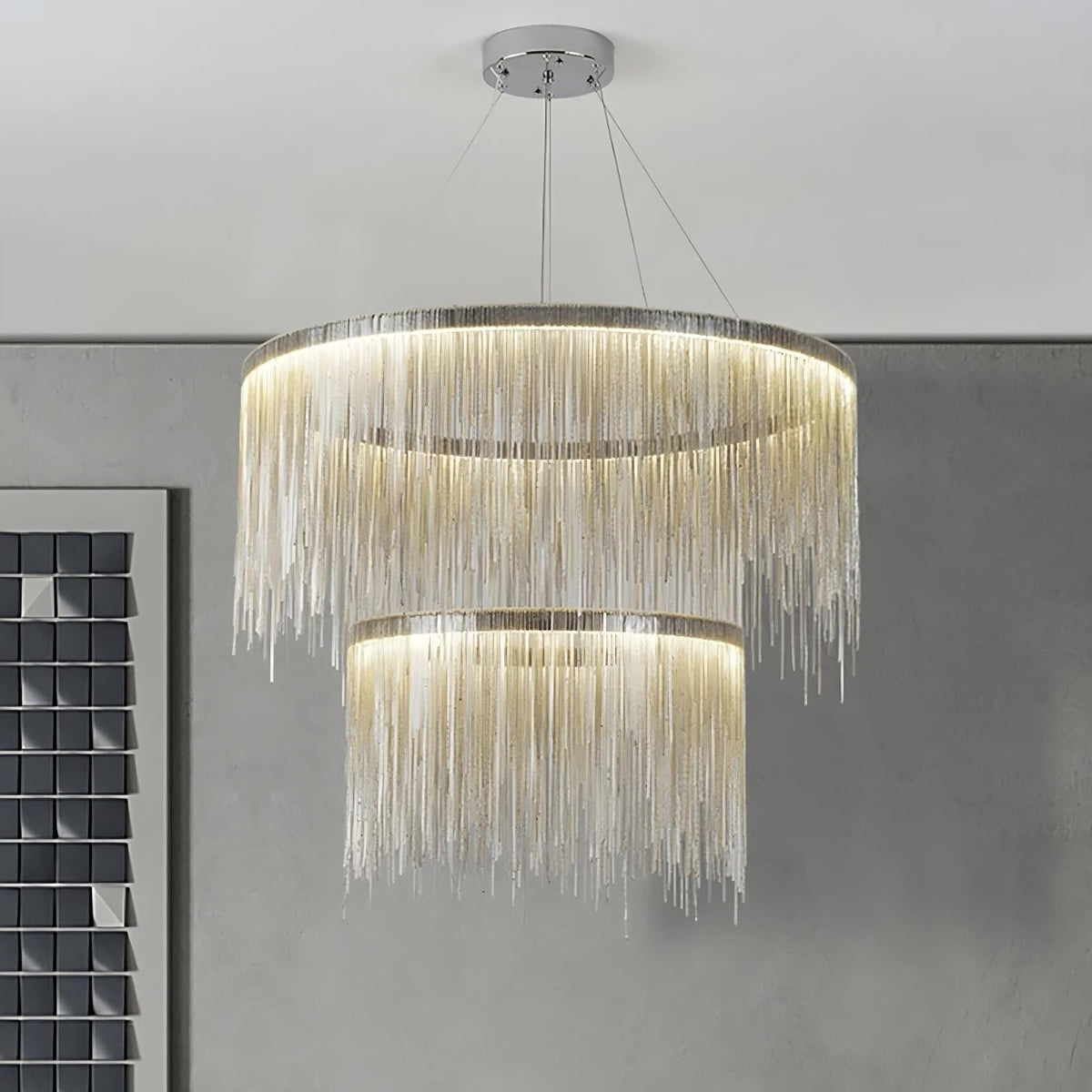 The Cadena Steel Tassel Modern Chandelier by Morsale.com, featuring multiple layers of cascading thin golden chains in a large circular design, serves as the focal point with its sleek LED light source. The backdrop of marble walls with a white and gray veined pattern underscores the elegance of the modern interior design.