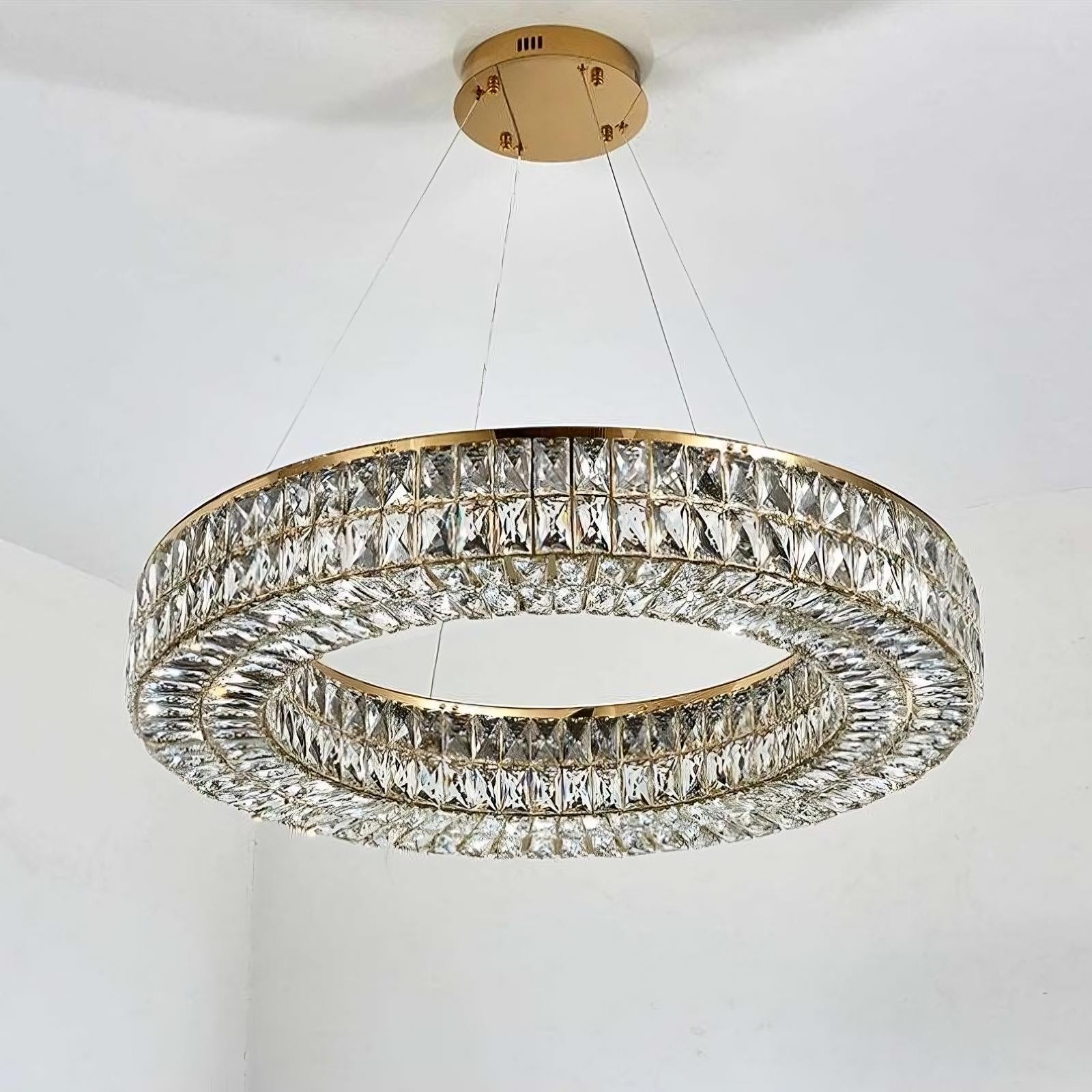 A Bacci Crystal Modern Chandelier, Gold hangs from the ceiling, featuring a double ring design with gold trim and encrusted with numerous clear, faceted crystals. The rings are suspended by thin, nearly invisible wires, creating an elegant and luxurious appearance. Available exclusively at Morsale.com.