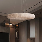 A Bergamo Crystal Modern Chandelier by Morsale.com, renowned for its luxurious finish, adorns the ceiling of a stylish room. This elegant space showcases wooden walls, ambient lighting, and minimalistic decor, all contributing to an atmosphere of sophistication.