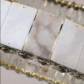 Close-up of a luxurious chandelier featuring rectangular marble-like panels with gold fixtures and a row of faceted crystal ornaments underneath. The panels display a blend of white and light grey tones, making this Natural Marble & Crystal Modern Ceiling Light Fixture from Morsale.com an elegant addition to any luxury home décor.