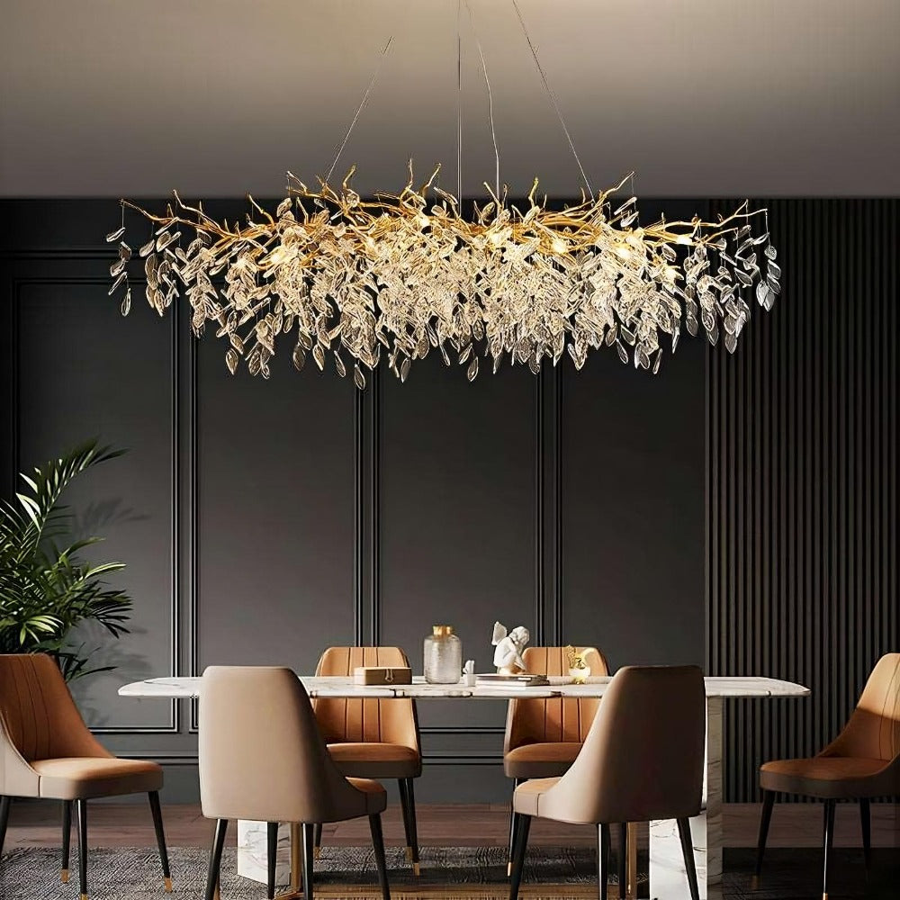 A modern dining room featuring an Albero Collection Crystal Chandelier by Morsale.com with leaf-like designs hanging above a sleek white dining table surrounded by beige chairs, against a dark gray paneled wall.