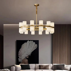 A contemporary living room radiates opulent allure with the Morsale Moonshade Marble & Copper Chandelier, featuring frosted glass shades that provide abundant illumination. Beneath it, a sectional sofa rests against vertical wooden panels and highlights a large piece of art showcasing a person wearing an intricate feathered headdress.