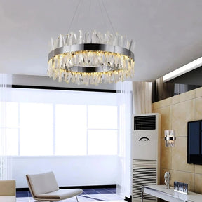 A modern living room featuring the Morsale.com Calvi Crystal Modern Chandelier with irregular clear crystal decorations hanging from the ceiling. The space includes a beige armchair, a white sofa, a flat-screen TV mounted on the wall, and an air conditioner placed next to the TV.