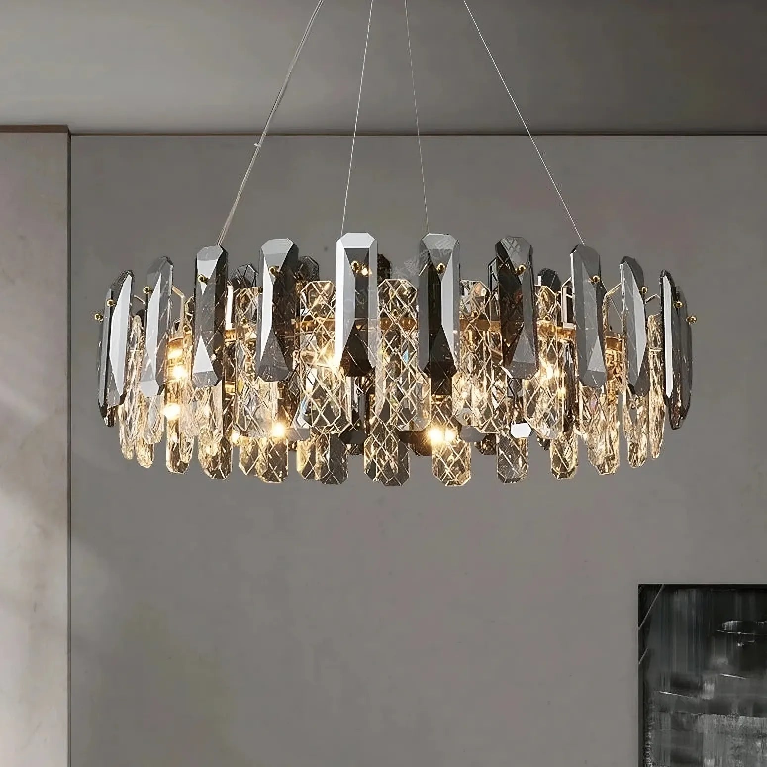 The Lazzo Crystal Ceiling Chandelier from Morsale.com hangs from the ceiling, featuring multiple elongated, faceted crystal pendants arranged in a circular pattern. The crystals reflect LED lighting, creating a dazzling effect against the minimalist, neutral-colored interior wall.