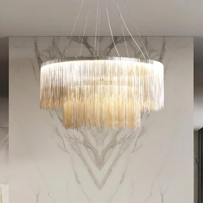 The Cadena Steel Tassel Modern Chandelier by Morsale.com, featuring multiple layers of cascading thin golden chains in a large circular design, serves as the focal point with its sleek LED light source. The backdrop of marble walls with a white and gray veined pattern underscores the elegance of the modern interior design.