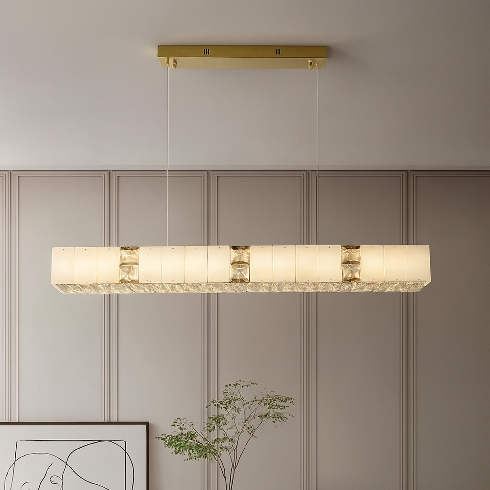 
                  
                    The Kolia Stafford Marble & Crystal Ceiling Chandelier hangs in a neutral room with paneled walls and minimalist decor, showcasing its elegant gold frame and frosted glass panels.
                  
                