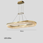 The Bergamo Crystal Dining Room Chandelier by Morsale.com is a modern ceiling fixture with a gold oval design featuring integrated 200W LED strip lighting and crystal accents, suspended by thin cables. It measures 90 cm in length, elegantly illuminating any space.