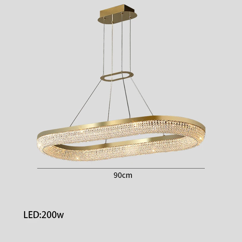 The Bergamo Crystal Dining Room Chandelier by Morsale.com is a modern ceiling fixture with a gold oval design featuring integrated 200W LED strip lighting and crystal accents, suspended by thin cables. It measures 90 cm in length, elegantly illuminating any space.