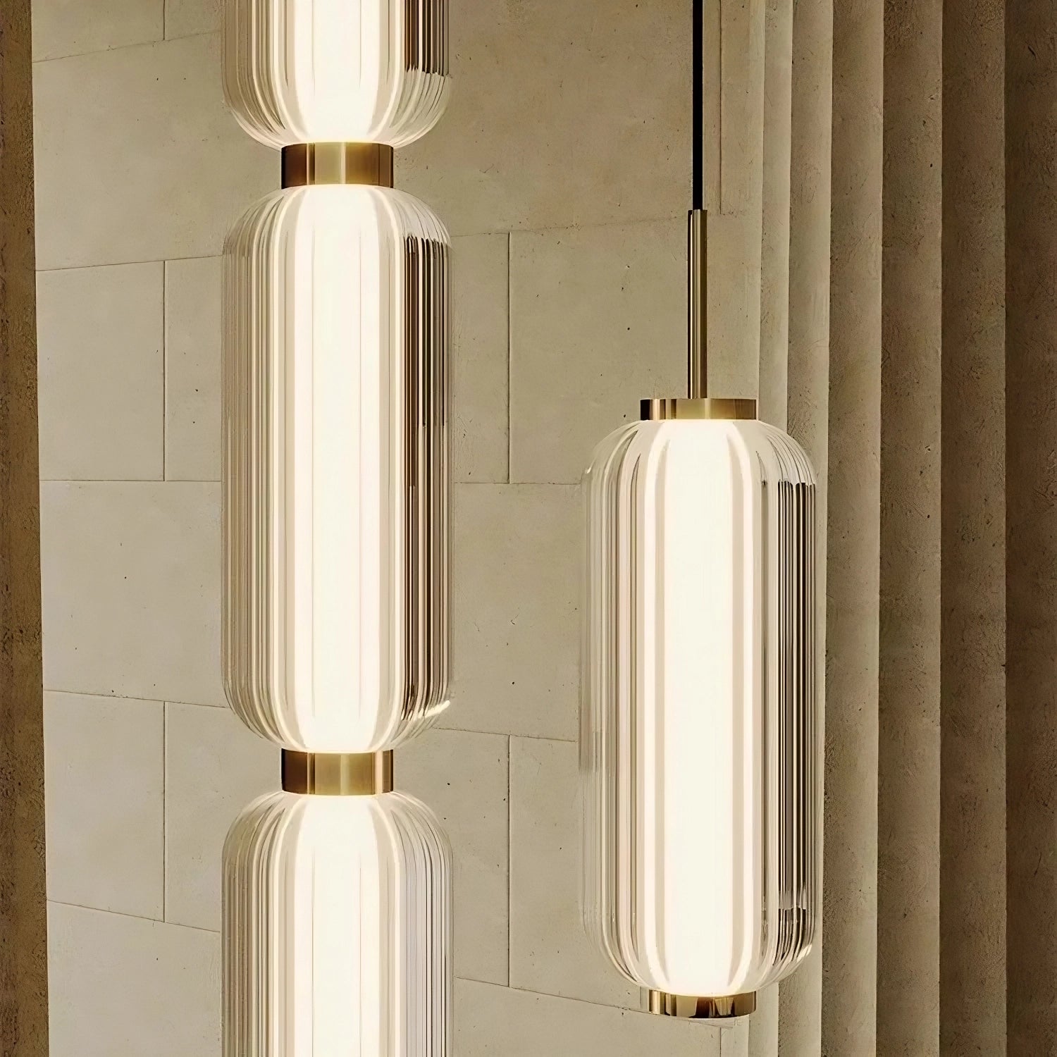 A vertical arrangement of Morsale.com's Modern Minimalist LED Pendant Light Fixtures with ribbed glass and brass accents is suspended against a textured stone wall. These pendant mount lights emit a warm, ambient glow, creating a sophisticated and elegant atmosphere reminiscent of classic marble chandeliers.