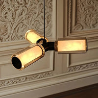 The Lumière Marble & Glass Pendant by Morsale features three gold-framed rectangular shades and hangs elegantly before a carved wall panel, casting a warm, soft glow that enhances any sophisticated space.