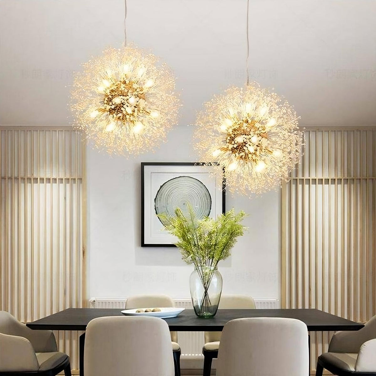 Two ornate Morsale.com Crystal Dandelion Sphere Ceiling Lights hang above a dining table, casting a warm glow over a minimalist room with beige walls, modern art, and a vase of greenery.