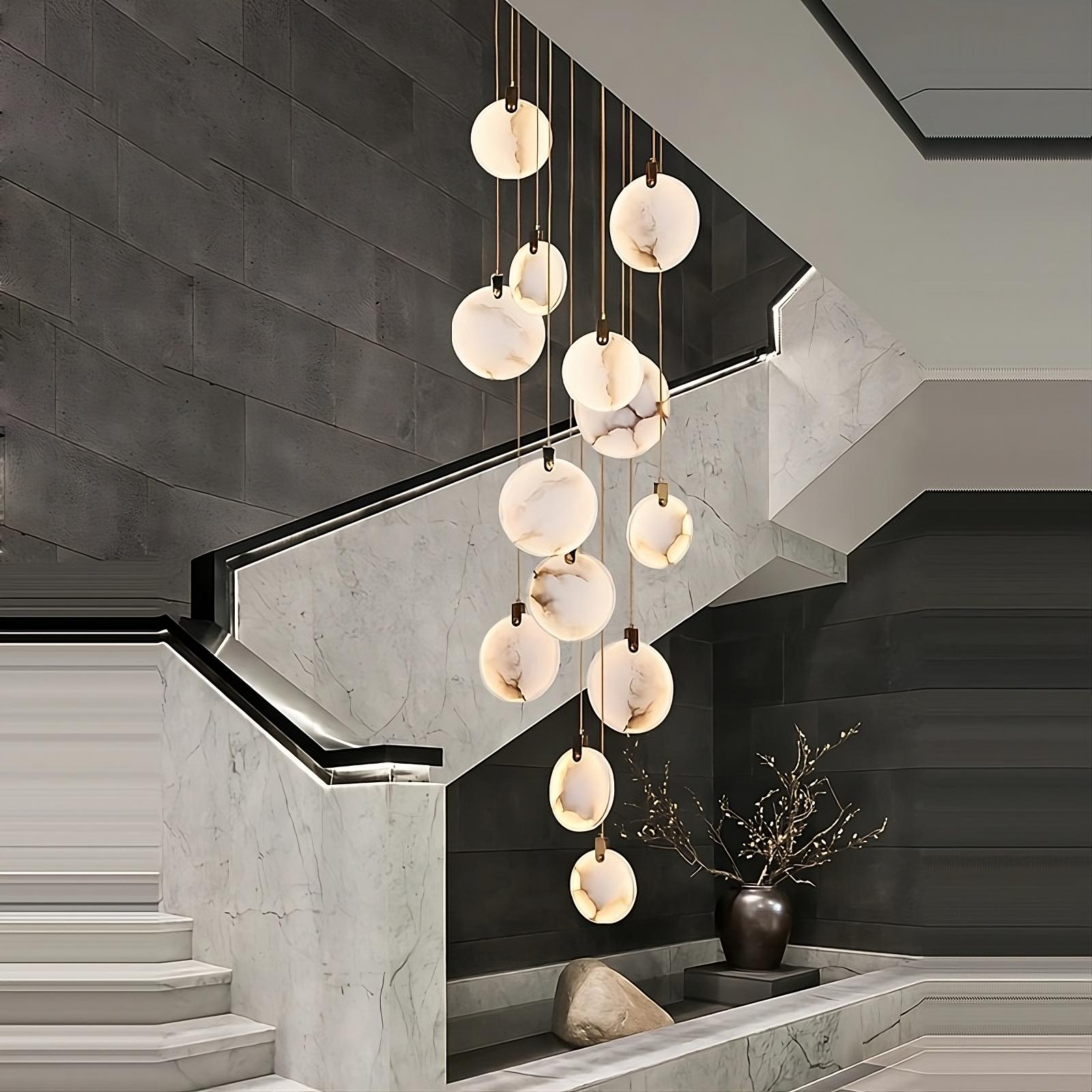 A modern marble staircase with the stunning Moonshade Natural Marble Pendant Light Fixture by Morsale.com, featuring pendant lights hanging at varying heights. A dark wall and a decorative vase with branches enhance the sophisticated and minimalist style of the space, perfectly embodying modern elegant lighting.