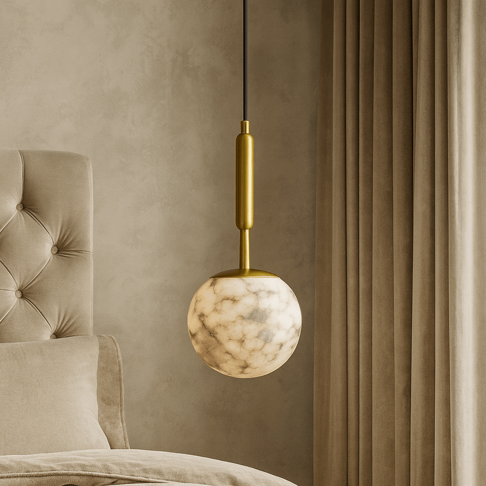 A modern bedroom features a tufted beige headboard, soft bedding, and the Morsale Solara Marble Orb Pendant with a gold fixture, hanging beside floor-length beige curtains.