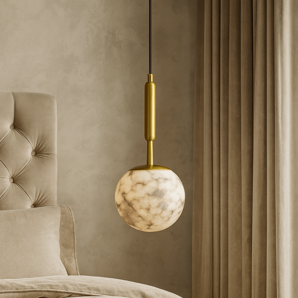 A modern bedroom features a tufted beige headboard, soft bedding, and the Morsale Solara Marble Orb Pendant with a gold fixture, hanging beside floor-length beige curtains.