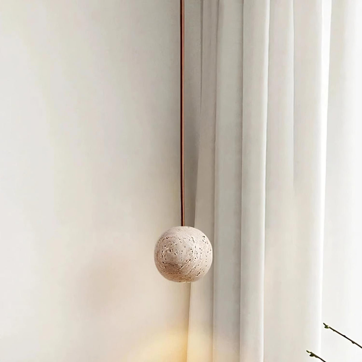 The Travertine Ball Pendant Light Fixture from Morsale.com, crafted from natural travertine stone, features a beige, porous surface that exudes a rustic and organic charm as it hangs from the ceiling. This elegant light fixture is suspended by a brown cord against a plain, off-white background.