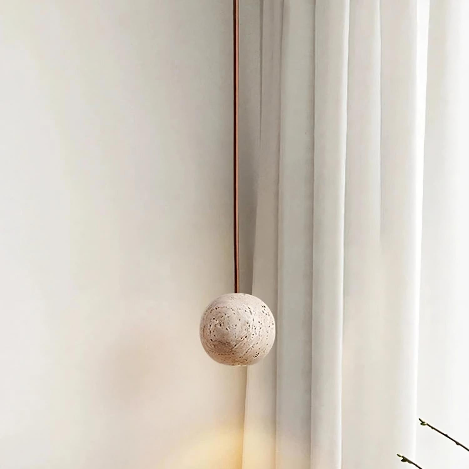 The Travertine Ball Pendant Light Fixture from Morsale.com, crafted from natural travertine stone, features a beige, porous surface that exudes a rustic and organic charm as it hangs from the ceiling. This elegant light fixture is suspended by a brown cord against a plain, off-white background.