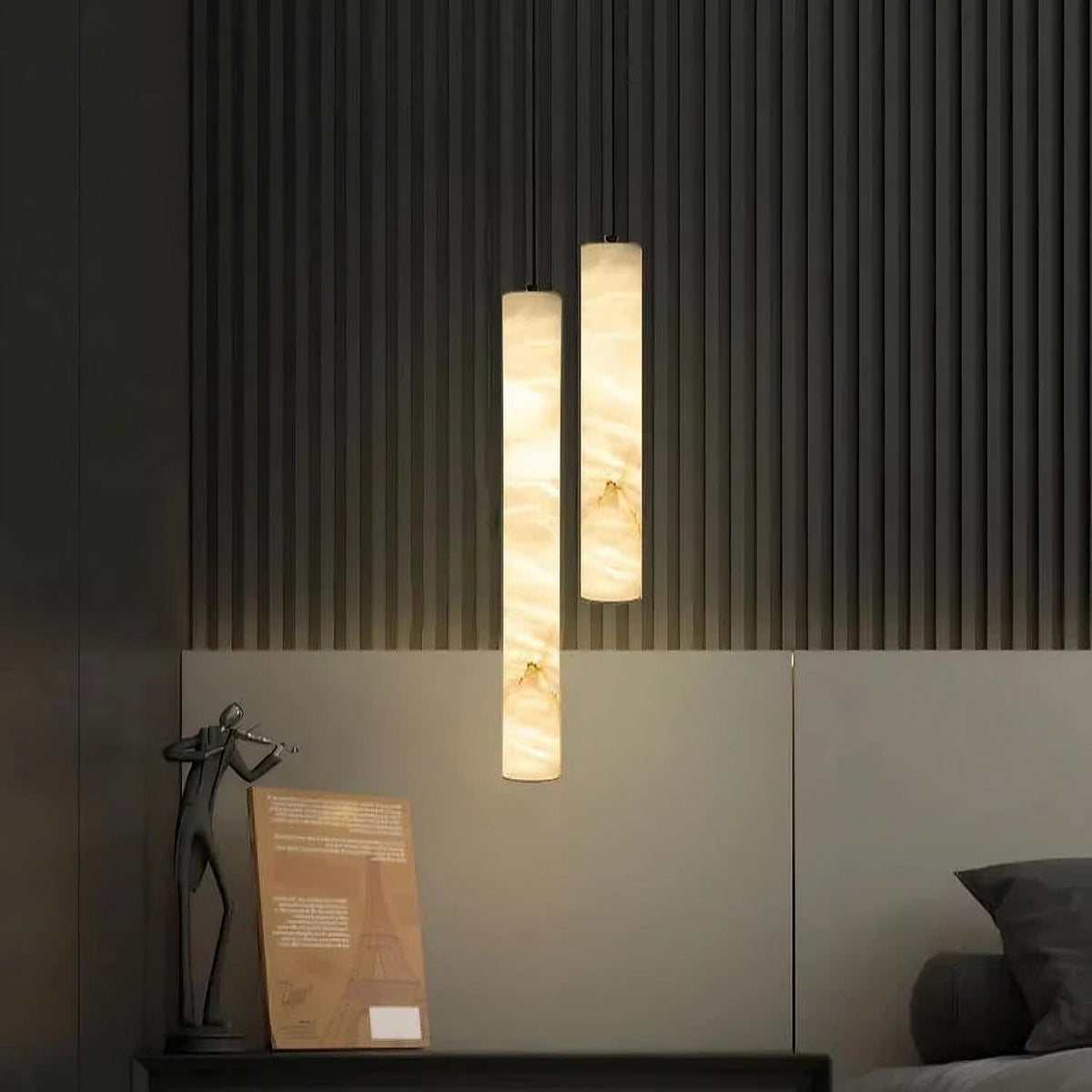 Two Moonshade Marble Lights by Morsale, emitting a warm glow, hang against a textured dark wall above a bed. A modern sculpture and framed picture rest on a nearby surface, adding to the chic contemporary decor, all enhanced by dimmable LED lighting perfect for setting the mood.