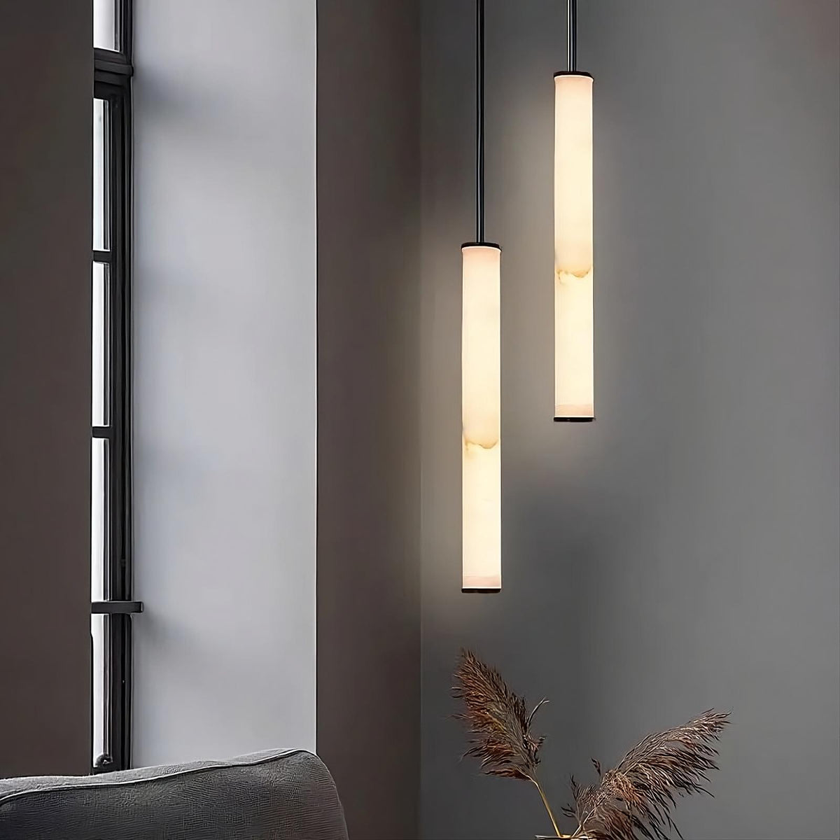 A sophisticated Cylindrical LED Pendant Lamp from Morsale.com, featuring a modern slim design with natural marble and black brass accents, is suspended against a grey wall with wooden paneling. The lamp casts a soft, ambient glow throughout the room. Below this elegant lighting fixture, there is a wall switch equipped with buttons and a digital display.