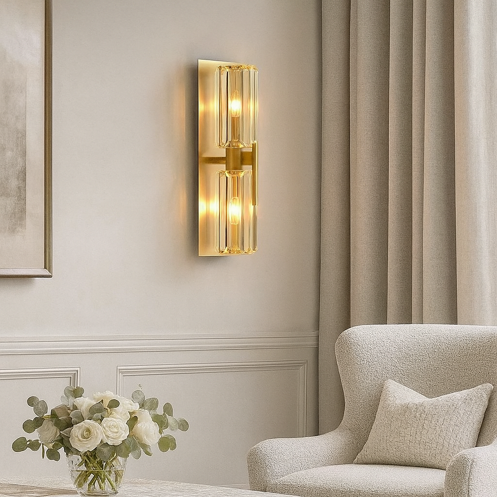 
                  
                    The Morsale Gio Crystal Sconce, featuring vertical glass panels, casts warm light above a white armchair with a pillow. A round table with a vase of white flowers sits beside the chair, while beige curtains softly frame the scene.
                  
                