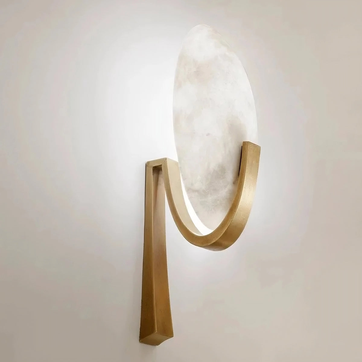 A Natural Marble & Copper Sconce Light from Morsale.com mounted on a beige wall. The handcrafted, gold U-shaped frame supports a large, round, white alabaster shade, seamlessly blending contemporary and minimalist aesthetics. The design provides soft, ambient light with integrated LED technology.