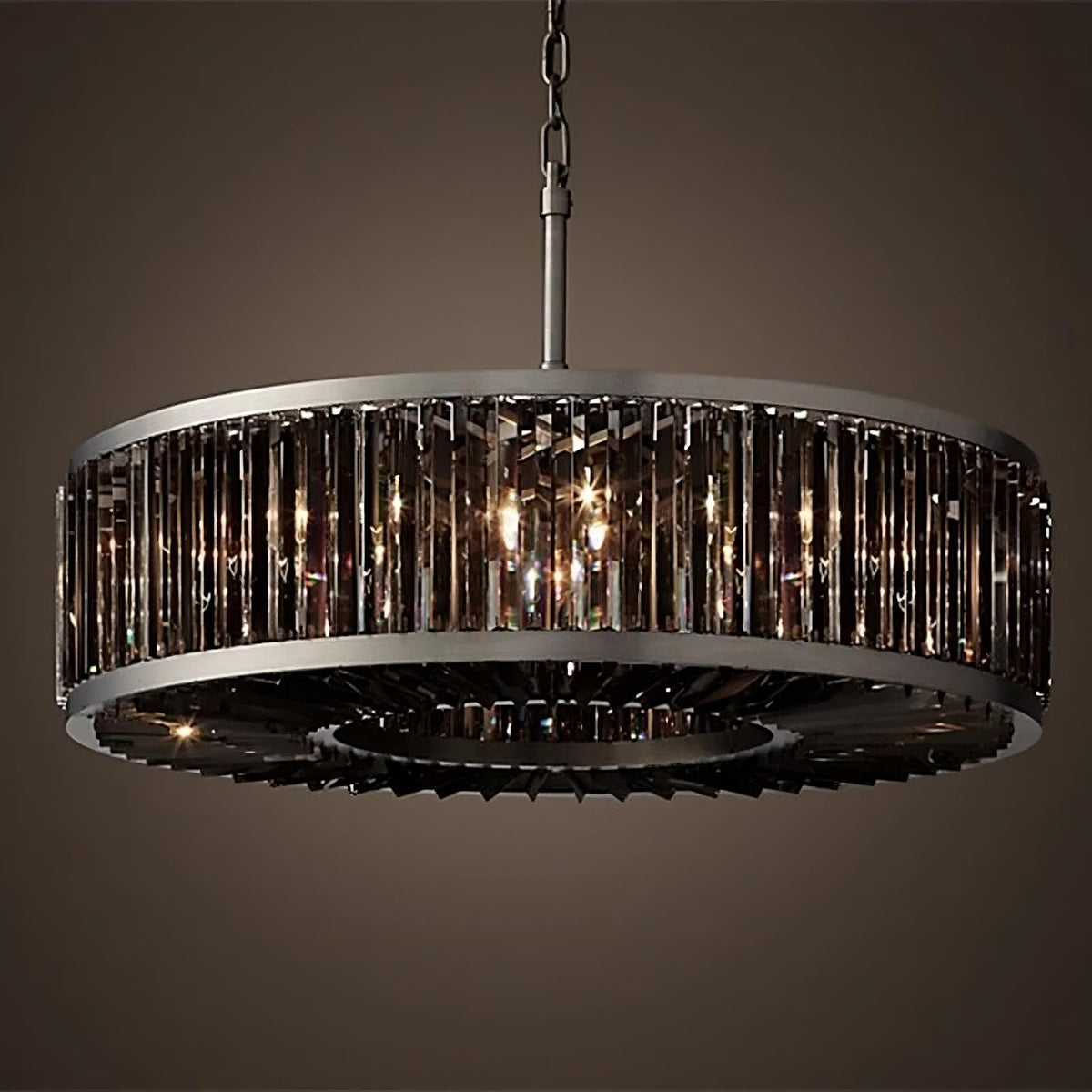 A modern, circular Gio Crystal Modern Chandelier with an industrial design hangs from a chain. The chandelier features a metal frame with vertical, rectangular glass panels surrounding the light bulbs, casting a warm, ambient glow. The background is dark, emphasizing the modern elegance of the chandelier by Morsale.com.