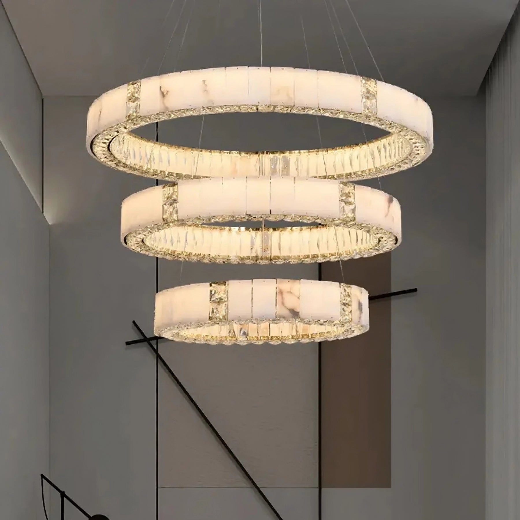 A Morsale.com Marble & Crystal Modern Chandelier featuring three large, illuminated circular rings suspended at descending heights. The rings are adorned with a natural marble-like finish interspersed with textured, translucent segments, casting a soft, ambient glow in an elegant room.
