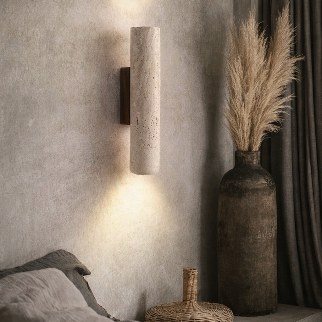 The Lunaro Travertine Wall Sconce by YEBMLP casts light up and down a textured beige wall, while a tall vase with pampas grass and dark drapes enhance the cozy, minimalist vibe of the softly neutral room.