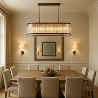 A modern dining room features a wooden table with eight beige upholstered chairs, a fruit bowl centerpiece, elegant wall sconces, a framed mirror, and the Gio Amber Crystal Dining Chandelier by Morsale.com overhead.