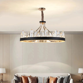 A modern living room features a white sofa adorned with brown, white, and patterned pillows. A round coffee table holds decorative items. The Villa Contemporary Chandelier by Morsale.com, boasting luxury lighting and large clear crystals, hangs from the ceiling, casting a warm light over the room. Two matching floor lamps flank the sofa.