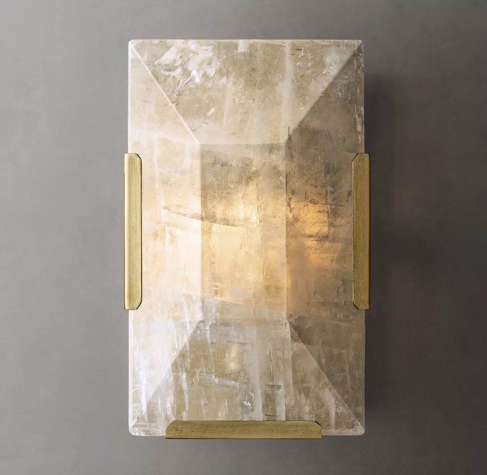 
                  
                    The Brookhill Calcite Crystal Sconce by Morsale.com features a faceted crystal shade and brass accents, emitting warm light. Its iron frame, mounted on a gray wall, adds elegance to any space.
                  
                