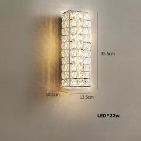 A modern, rectangular wall light with a grid design and smoke grey crystals. The stainless steel body is illuminated and mounted on a plain wall. Dimensions are 35.5 cm in height, 13.5 cm in width, and 10.5 cm in depth. Text indicates "LED*22w". Introducing the Bacci Clear Crystal Light Fixture by Morsale.com.
