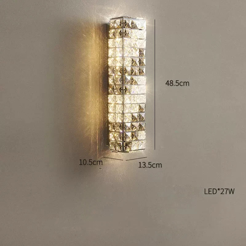 A Morsale Bacci Smoke & Clear Crystal Wall Sconce with a geometrically patterned glass design is mounted on a wall. Featuring integrated LED technology, the fixture measures 48.5 cm in height, 13.5 cm in width, and 10.5 cm in depth, and uses a 27W LED bulb for sustainable lighting.