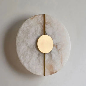 The Morsale Moonshade Natural Marble & Copper Wall Sconce features a minimalist design with a modern flair, boasting a large stone-finished disc highlighted by a smaller central copper circle and an elegant vertical copper line. Its soft, neutral color palette perfectly complements the sophisticated touch of natural marble elements.