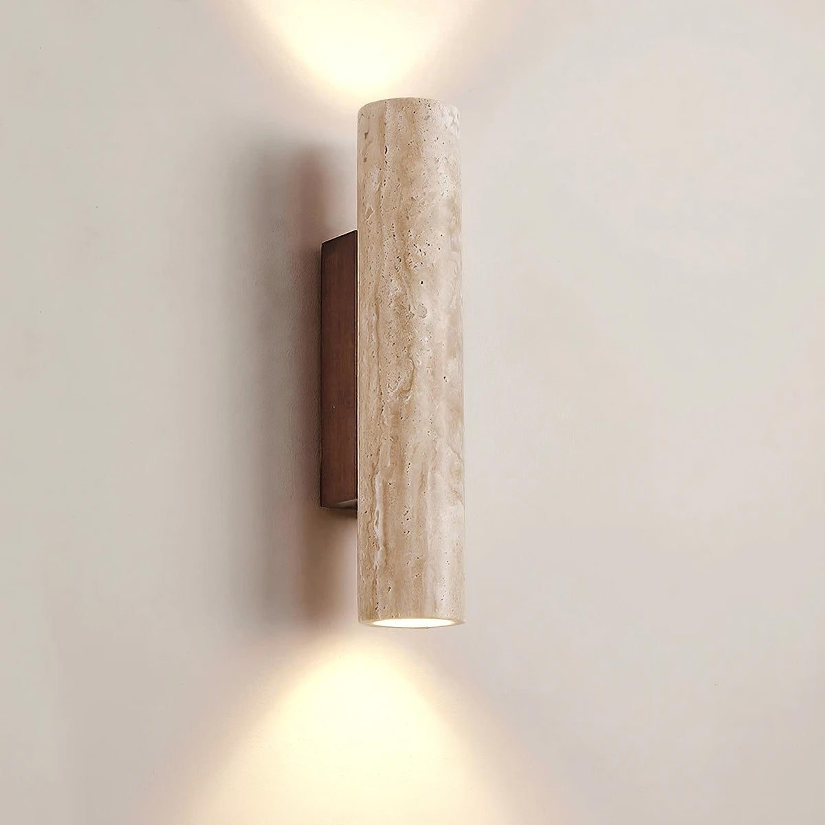 The YEBMLP Natural Travertine Wall Lamp, made of light-colored, textured stone, emits light from both the top and bottom. It is mounted on a rectangular wooden backplate attached to a beige wall, enhanced by ribbed champagne glass accents, creating a soft, ambient lighting effect.