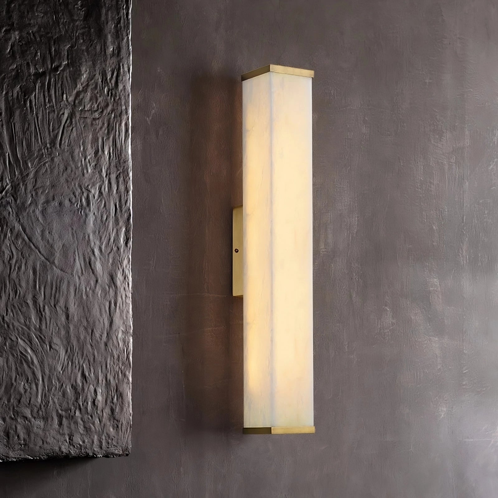 A modern, rectangular marble LED sconce with a soft white glow is mounted on a textured dark gray wall. The Natural Marble Indoor Wall Sconce Light by Morsale.com boasts a sleek, minimalist design featuring a central vertical support.