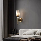 The Palermo Copper & Glass Contemporary Wall Sconce by Morsale features a gold-colored base and a textured glass shade, illuminated with energy-efficient LED light. Crafted from copper, this sconce is mounted on a gray wall, offering a sleek and elegant appearance.