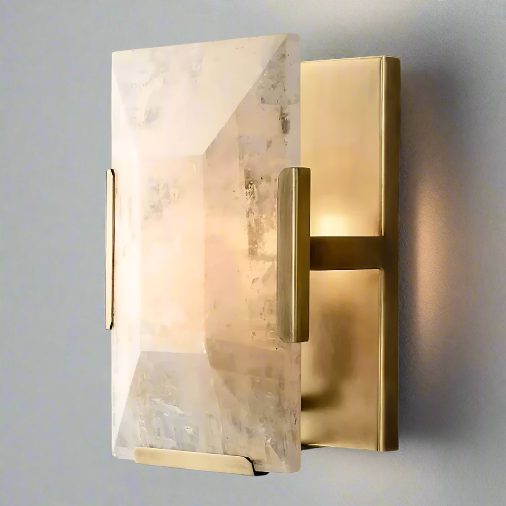 The Villano Calcite Crystal Wall Sconce by Morsale.com features a modern design with a rectangular brass base paired with a large, translucent, irregularly-shaped handcrafted crystal light cover. The internal light emits a soft, warm glow that beautifully illuminates the facets of the crystal. This elegant design adds an element of sophistication perfect for any interior decor.