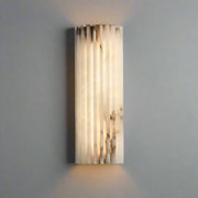 The Morsale Natural Marble LED Wall Sconce showcases a textured cylindrical design made from translucent marble, providing an elegant, warm glow against the gray textured wall.
