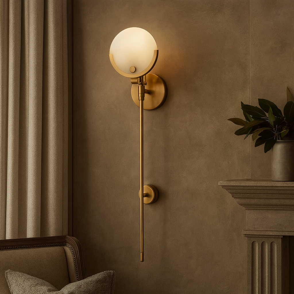The Terra Marble Wall Sconce by Morsale.com features a gold natural marble base, round frosted glass shade, and integrated LED, casting warm white light in an elegant living room beside gray curtains, a plant, and a fireplace mantel.