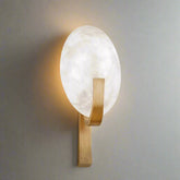 The Natural Marble & Copper Sconce Light by Morsale.com features a circular frosted glass light that emits a soft glow, supported by a sleek curved metal bracket in a matte gold finish, and mounted on a light gray wall. This modern and minimalist design is further enhanced with handcrafted natural marble accents, adding an elegant touch.