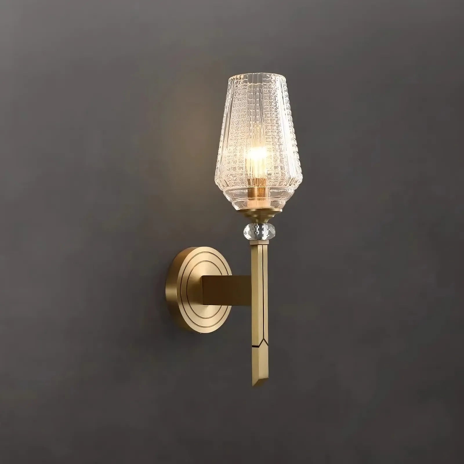 The Palermo Copper & Glass Contemporary Wall Sconce by Morsale features a gold-colored base and a textured glass shade, illuminated with energy-efficient LED light. Crafted from copper, this sconce is mounted on a gray wall, offering a sleek and elegant appearance.