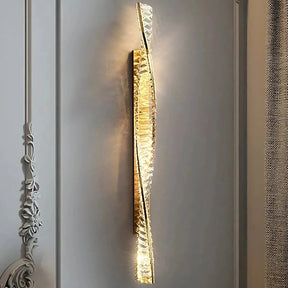 The Morsale Gio Crystal Sconce is a contemporary vertical wall lamp featuring a twisted metallic and glass design that casts a warm light. Its crystal accents add elegance, making it an ideal addition to sleek, minimalistic walls for enhancing the sophistication of interior decor.